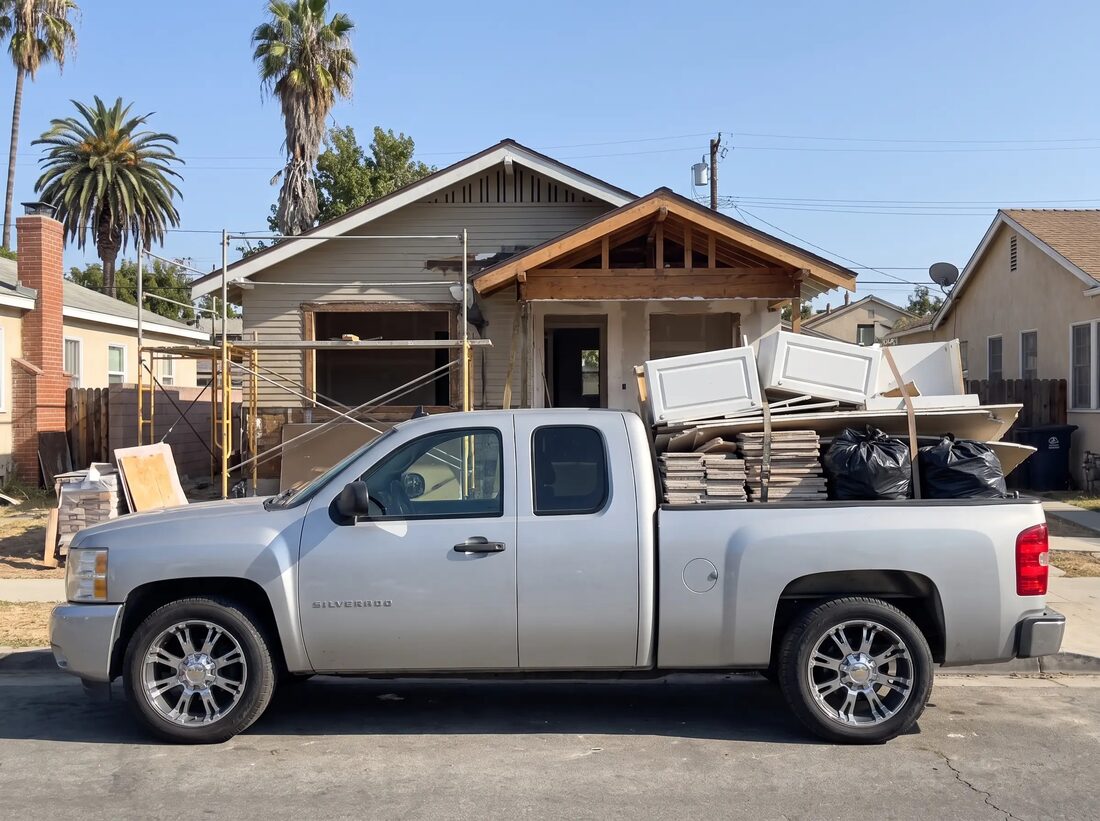 Silver Chevrolet Silverado loaded with torn-out cabinets, tile and contractor bags outside a house mid-remodel